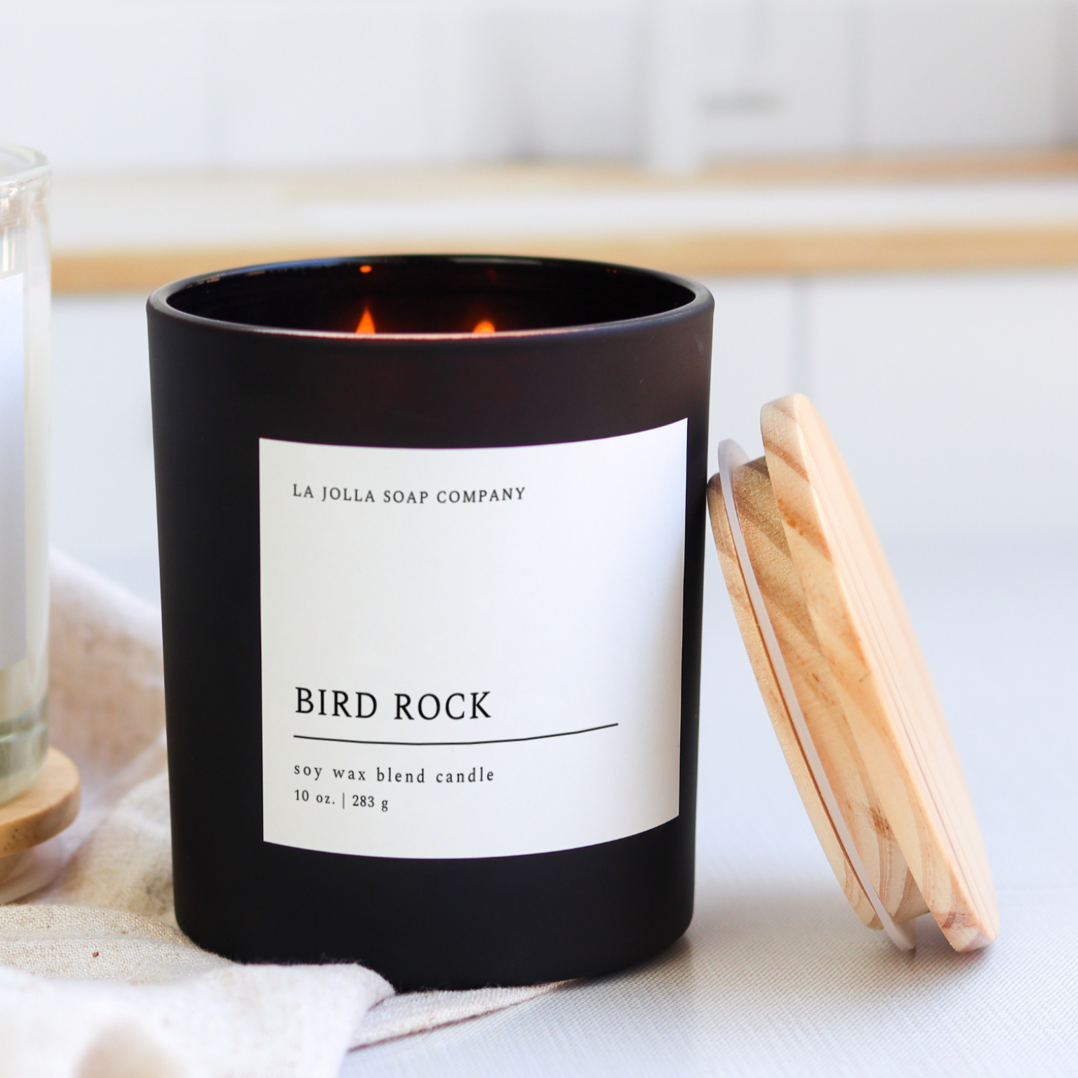Bird Rock Candle in a black glass jar, featuring scent notes of coconut, sandalwood, cedar, and tonka bean, inspired by the coastal charm of La Jolla's Bird Rock Area.