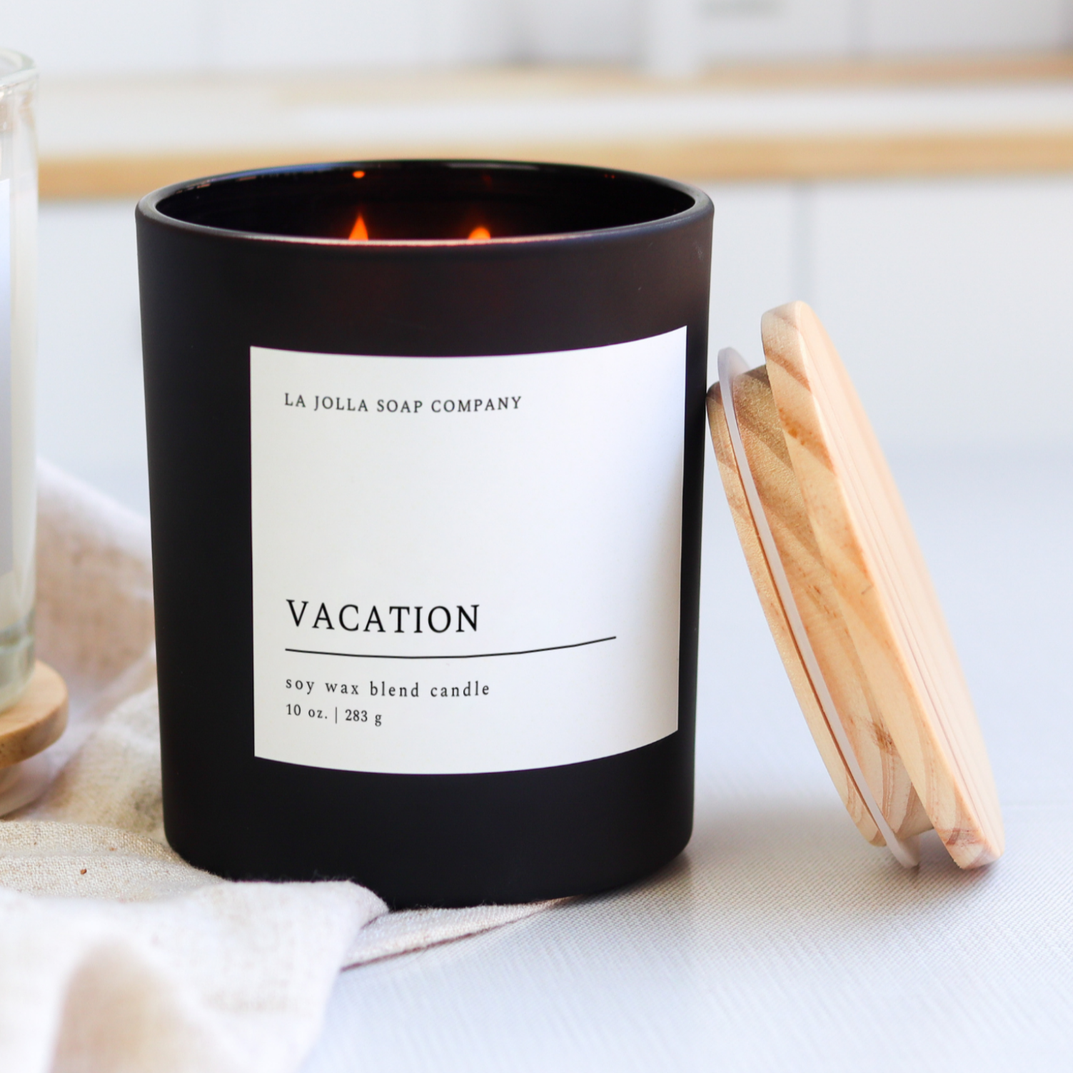 Vacation Candle 10 oz in Matte Black jar with a wood lid. This sensory experience is a soothing blend of oceanic aromas, highlighted by the warmth of cocoa butter, the sweetness of vanilla and the tropical essence of coconut. It evokes memories of a relaxing beach vacation, complete with the gentle caress of sea breezes and the indulgence of tropical delights.
