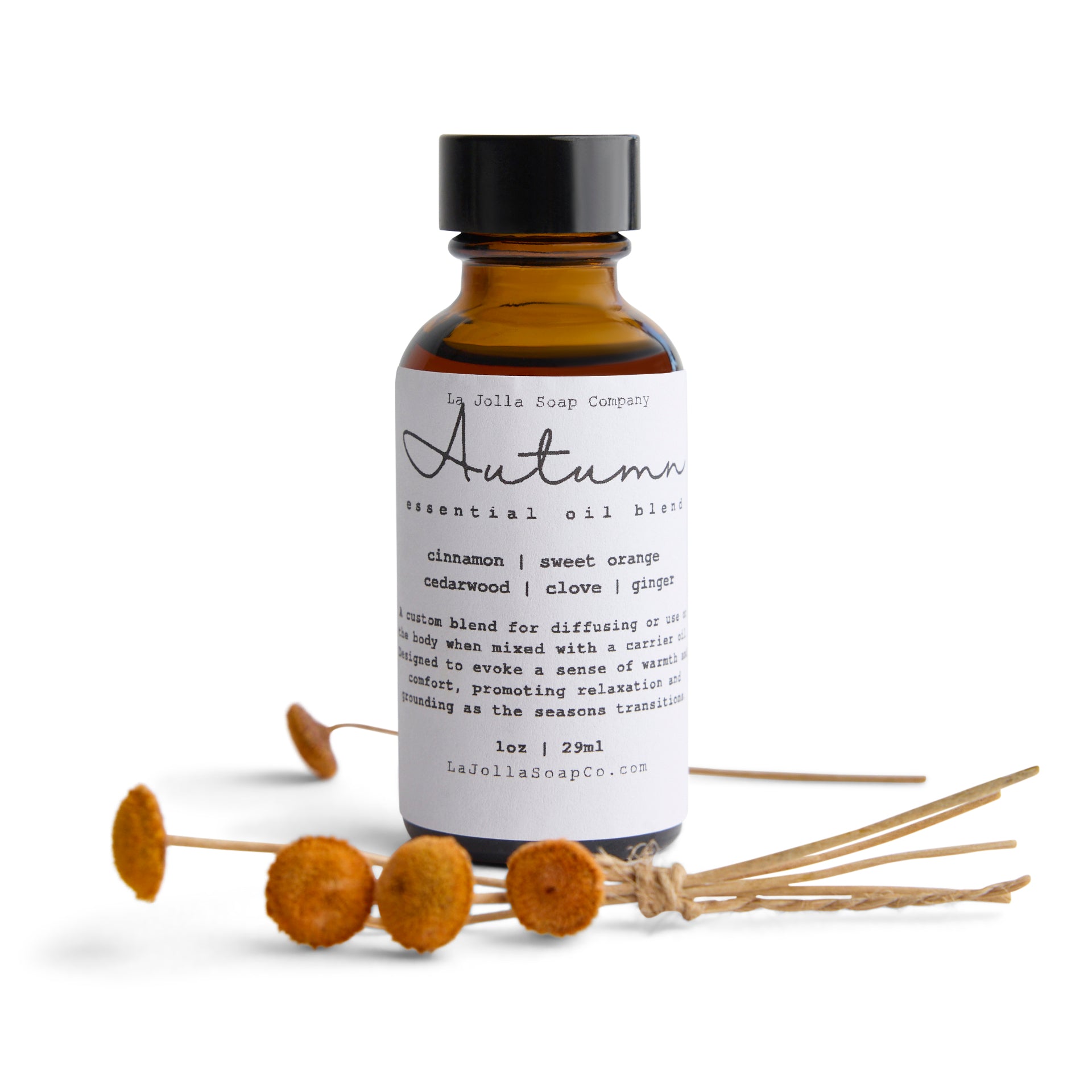 A bottle of Autumn essential oil blend with small orange button flowers laid in front. The blend evokes a warm and cozy seasonal vibe.