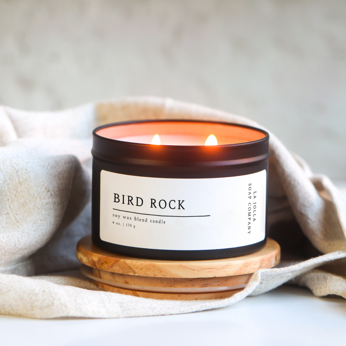 Bird Rock Candle in a black tin, featuring scent notes of coconut, sandalwood, cedar, and tonka bean, inspired by the coastal charm of La Jolla's Bird Rock Area.