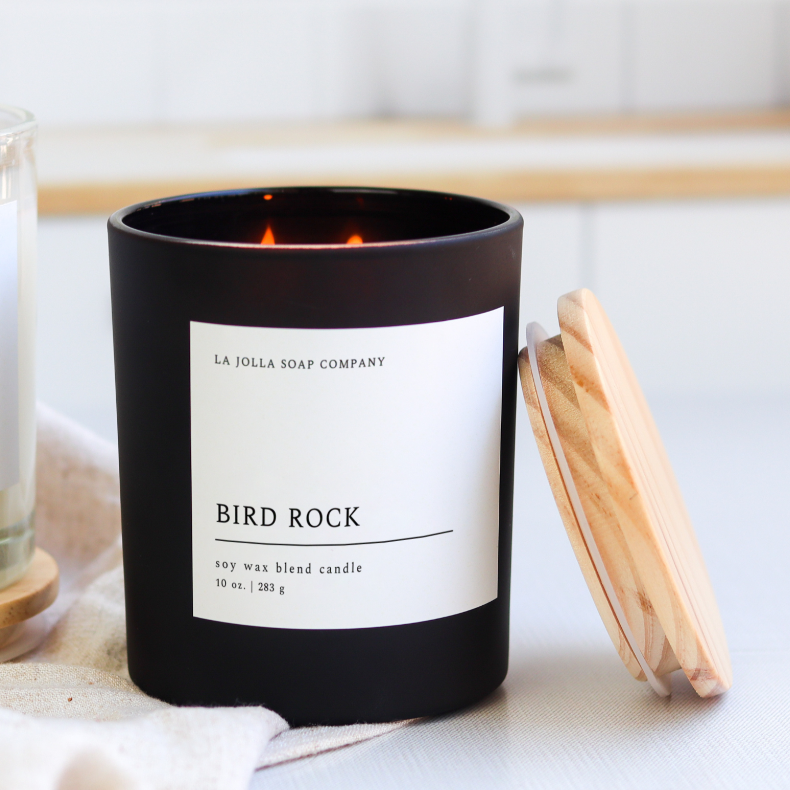 Bird Rock Candle in a black  glass jar, featuring scent notes of coconut, sandalwood, cedar, and tonka bean, inspired by the coastal charm of La Jolla's Bird Rock Area.