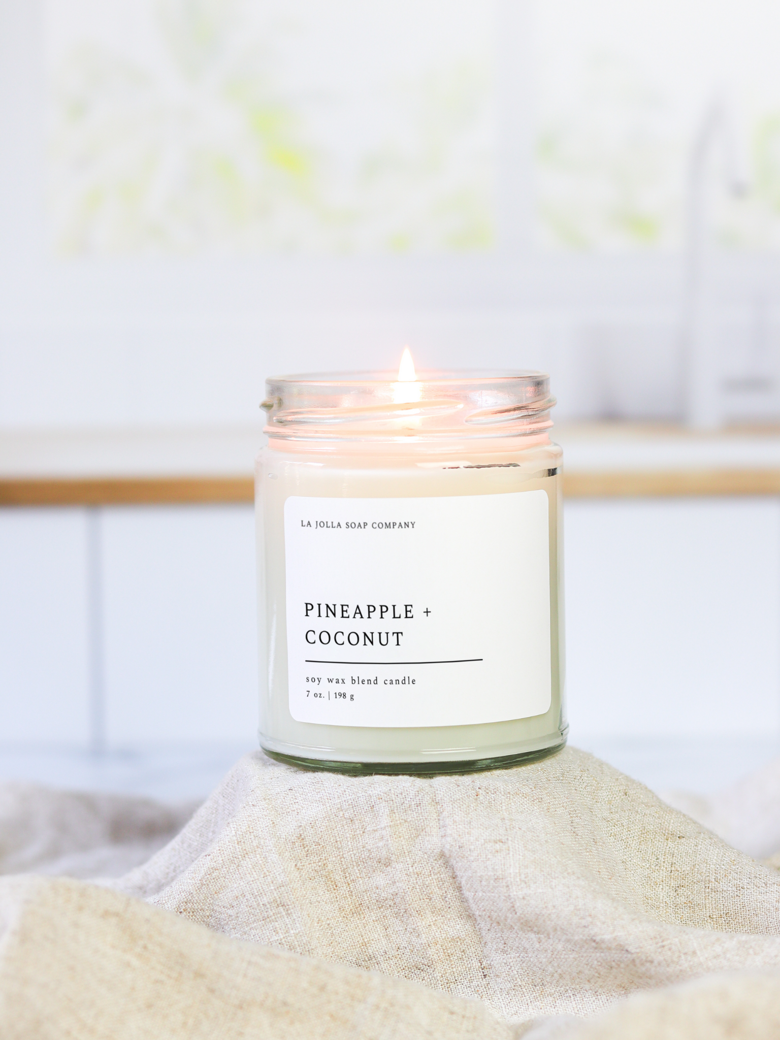 Pineapple Coconut 7 oz candle in a clear jar with a black metal lid. Pineapple and coconut, blended together in perfect harmony. The aroma conjures images of swaying palm trees and sun-drenched shores, offering a serene Tropical Paradise in your own home