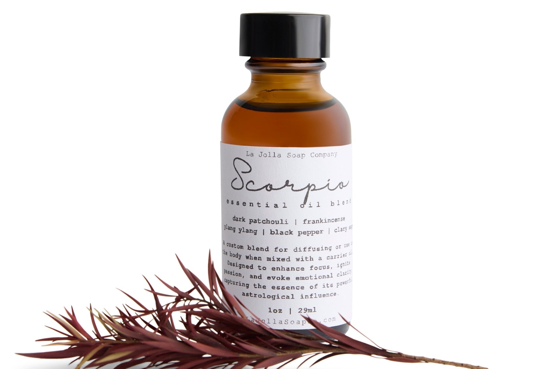 A bottle of Scorpio Essentia Oil Blend with a sprig of red colored long skinny, pointed leaves set against a clean, natural white background, creating a bold and dynamic visual.