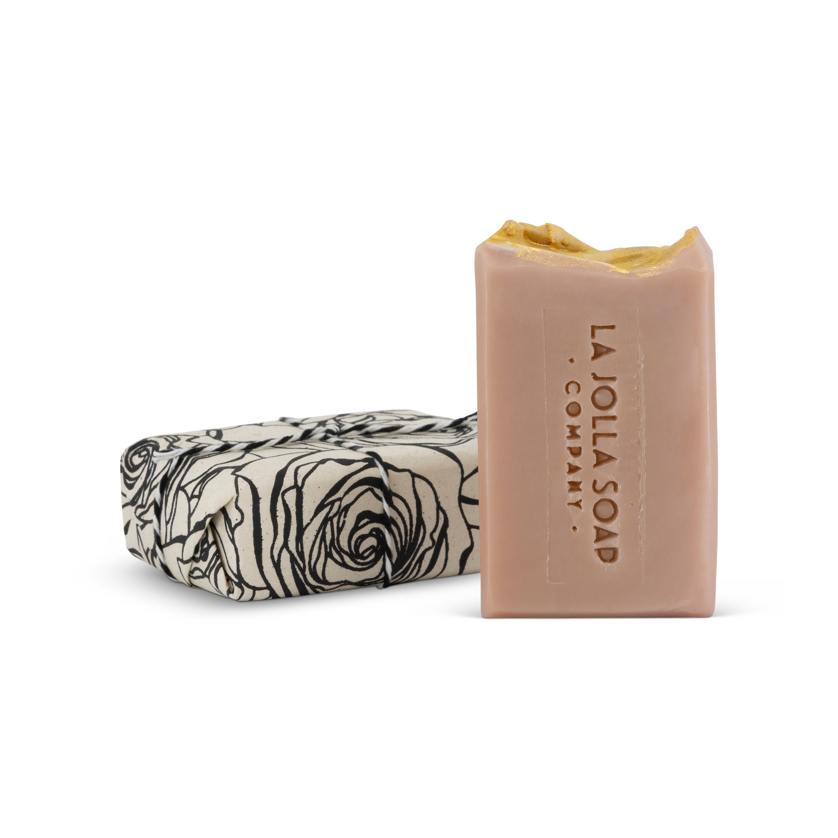 A la jolla soap company brand, lovely pink colored soap bar with one wrapped next to it in black and white rose printed paper, set on a clean white background.