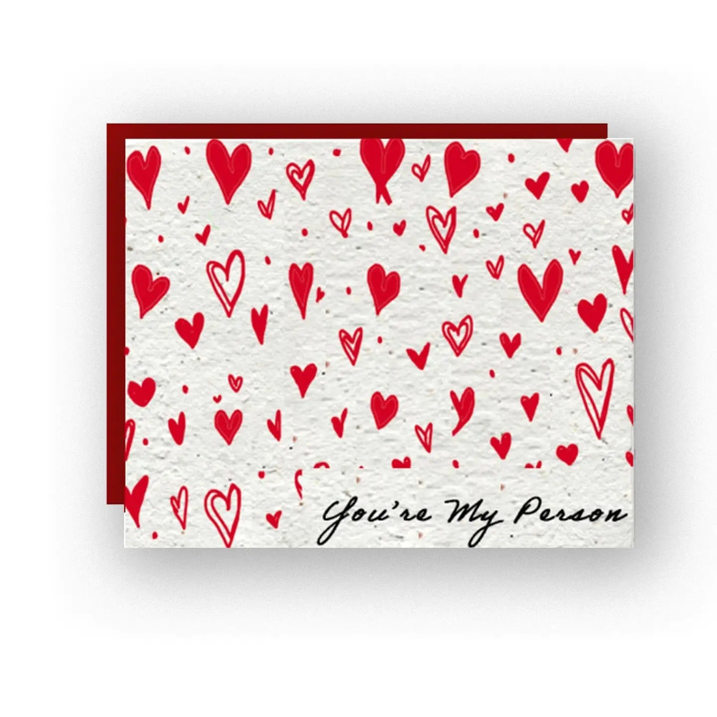 A  artisan card with little red hearts adorning the face of the card.  This card is embedded with wildflower seeds making the card plantable and the paper is also biodegradable.